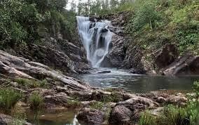 A picturesque waterfall cascading into a tranquil pool surrounded by rocky terrain and lush greenery.