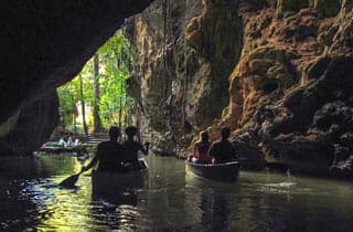 Kayakers paddling through a cave with lush greenery in the background.