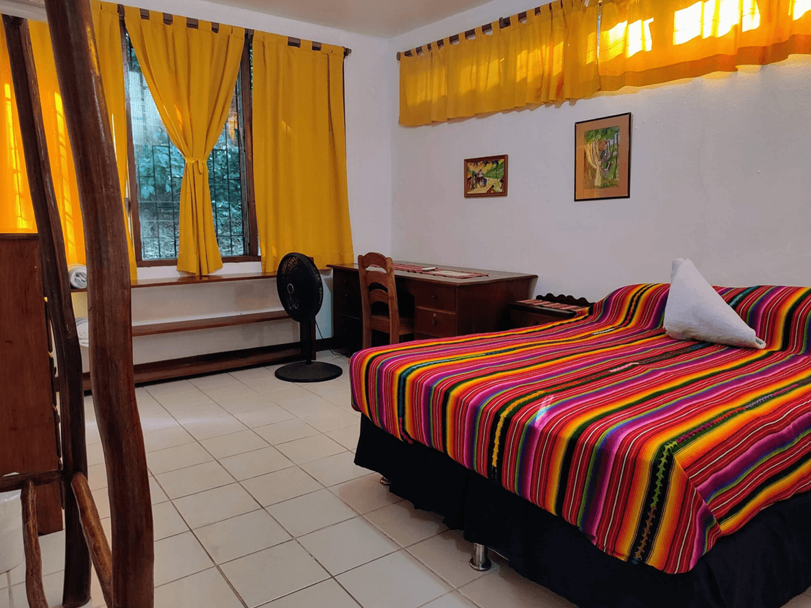 A cozy bedroom featuring a colorful striped bedspread, yellow curtains, and a desk.