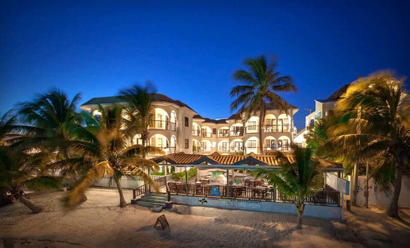 A beachfront hotel with palm trees under a twilight sky.