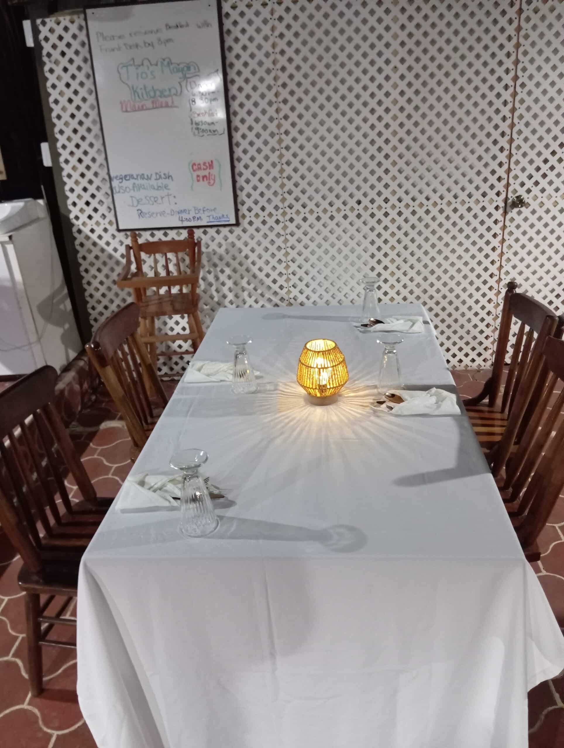 A neatly set dining table with a white tablecloth and a glowing lantern centerpiece.