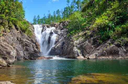 A serene waterfall cascading into a clear pool, surrounded by lush greenery and rocky cliffs.