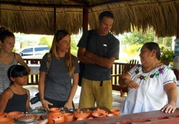 A group of four people engages in conversation with a woman at a market displaying pottery.