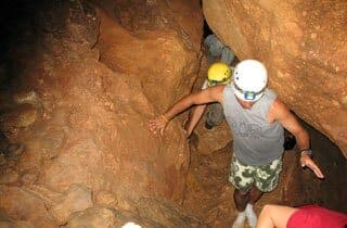 A group of cavers navigating through a narrow passage in a rock cave.